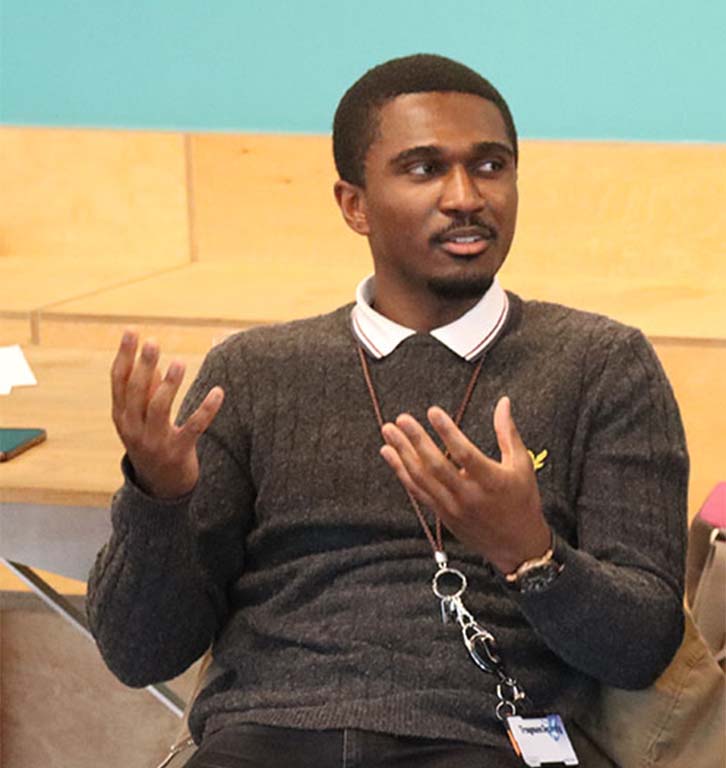 An image of a Black person sat down speaking to someone to their left, off camera.